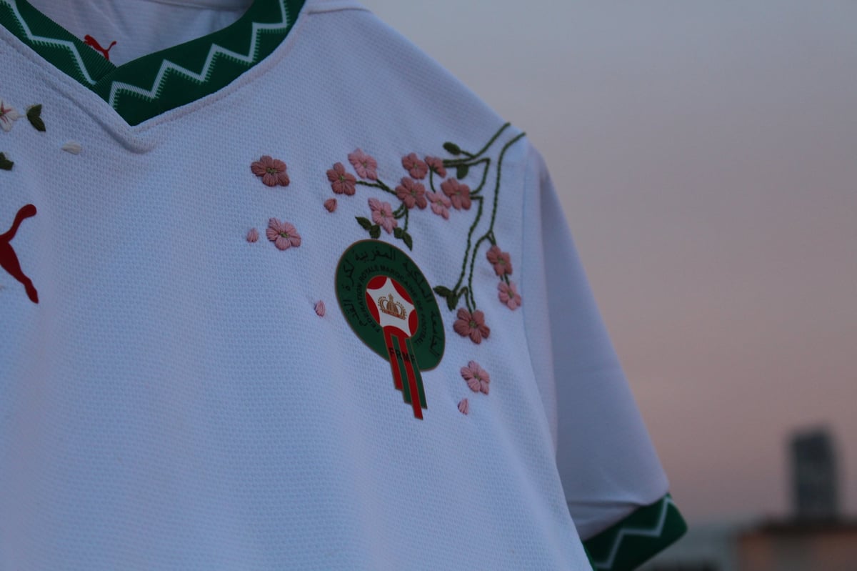 Close-up of a white long-sleeve shirt with embroidered holiday design featuring a wreath with red star and falling leaves