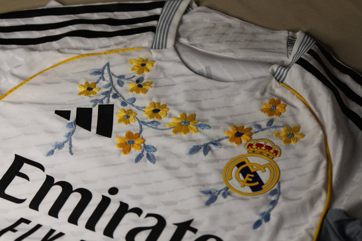 Close-up of white jersey showing decorative yellow flowers with blue leaves embroidered on the sleeve