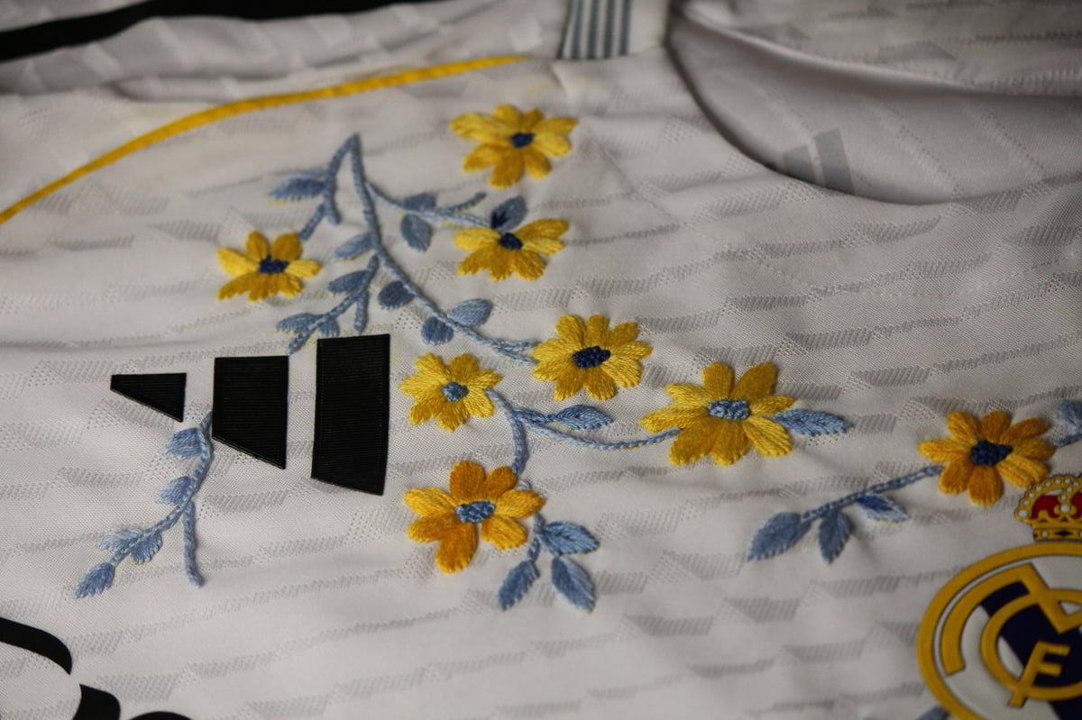 White fabric with embroidered yellow flowers and blue leaves, featuring a black geometric design element